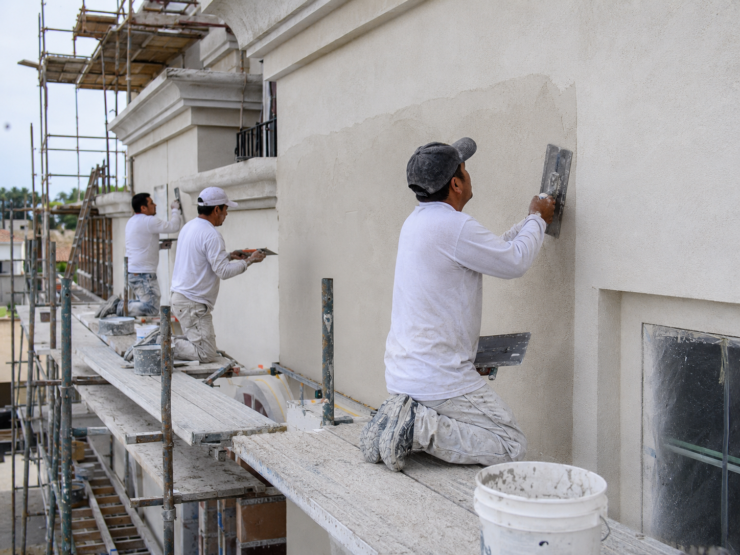 Stucco crew on scaffolding using trowels to apply and refine an exterior plaster finish